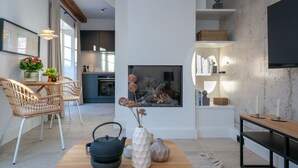 A modern living room with a fireplace, a dining area with wicker chairs, and a kitchen in the background. - NEU 2023 - Sylter Meerwind - NEU 2023 - Helle Zwei Zimmer Wohnung im Herzen von Alt Westerland (Sylt)