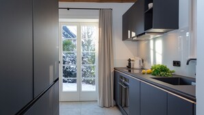A modern kitchen with grey cabinets, a stainless steel refrigerator, a built-in oven, and a sink. - NEU 2023 - Sylter Meerwind - NEU 2023 - Helle Zwei Zimmer Wohnung im Herzen von Alt Westerland (Sylt)