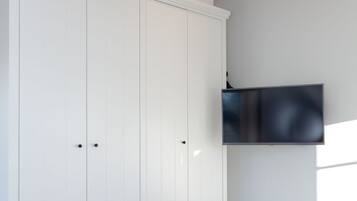 A bedroom with a bed, white wardrobe, and a mounted TV.
