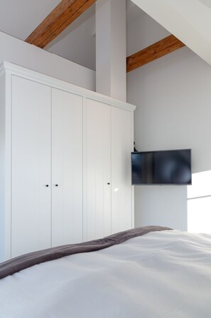 A bedroom with a bed, white wardrobe, and a mounted TV. - NEU 2023 - Sylter Meerwind - NEU 2023 - Helle Zwei Zimmer Wohnung im Herzen von Alt Westerland (Sylt)