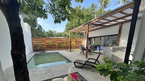 Un jardin avec une piscine, des chaises longues, une pergola en bois et un espace patio avec une table et des chaises.