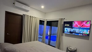Une chambre d’hôtel moderne avec un grand lit, un téléviseur fixé au mur et une vue sur une piscine depuis la fenêtre.