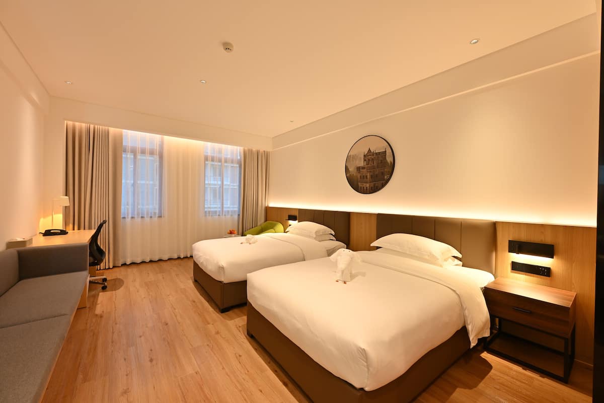 Habitación de hotel con dos camas, un escritorio, una silla y un ventanal con cortinas.