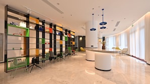 A modern hotel lobby with a central reception desk, colorful shelving units, and a variety of seating options. - Changsheng Hotel  (Jiangmen)