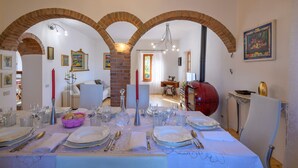 A dining area with a long table set for a meal, featuring a brick archway, a red stove, and a sewing machine in the background. - 3 bedroom amazing home in Montelabbate (Montelabbate)