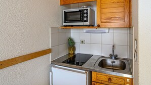 A compact kitchen with wooden cabinets, a microwave, a sink, and a small refrigerator.