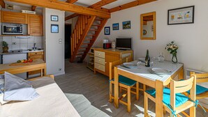 A cozy, well-lit room with wooden beams, a kitchenette, a dining area with a table and chairs, and a staircase leading to another level.