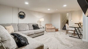 A living room with a grey sofa, a beige armchair, a glass-top table, and a lamp. - Bon Voyage (Colorado Springs)