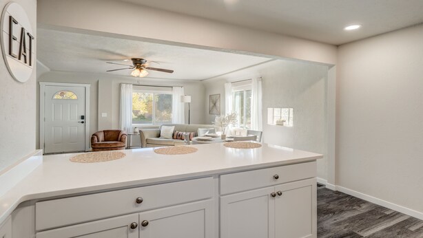 A modern kitchen with a large island, white cabinetry, and a ceiling fan. - Bon Voyage (Colorado Springs)