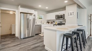 A modern kitchen with white cabinets, stainless steel appliances, and a central island with bar stools. - Bon Voyage (Colorado Springs)