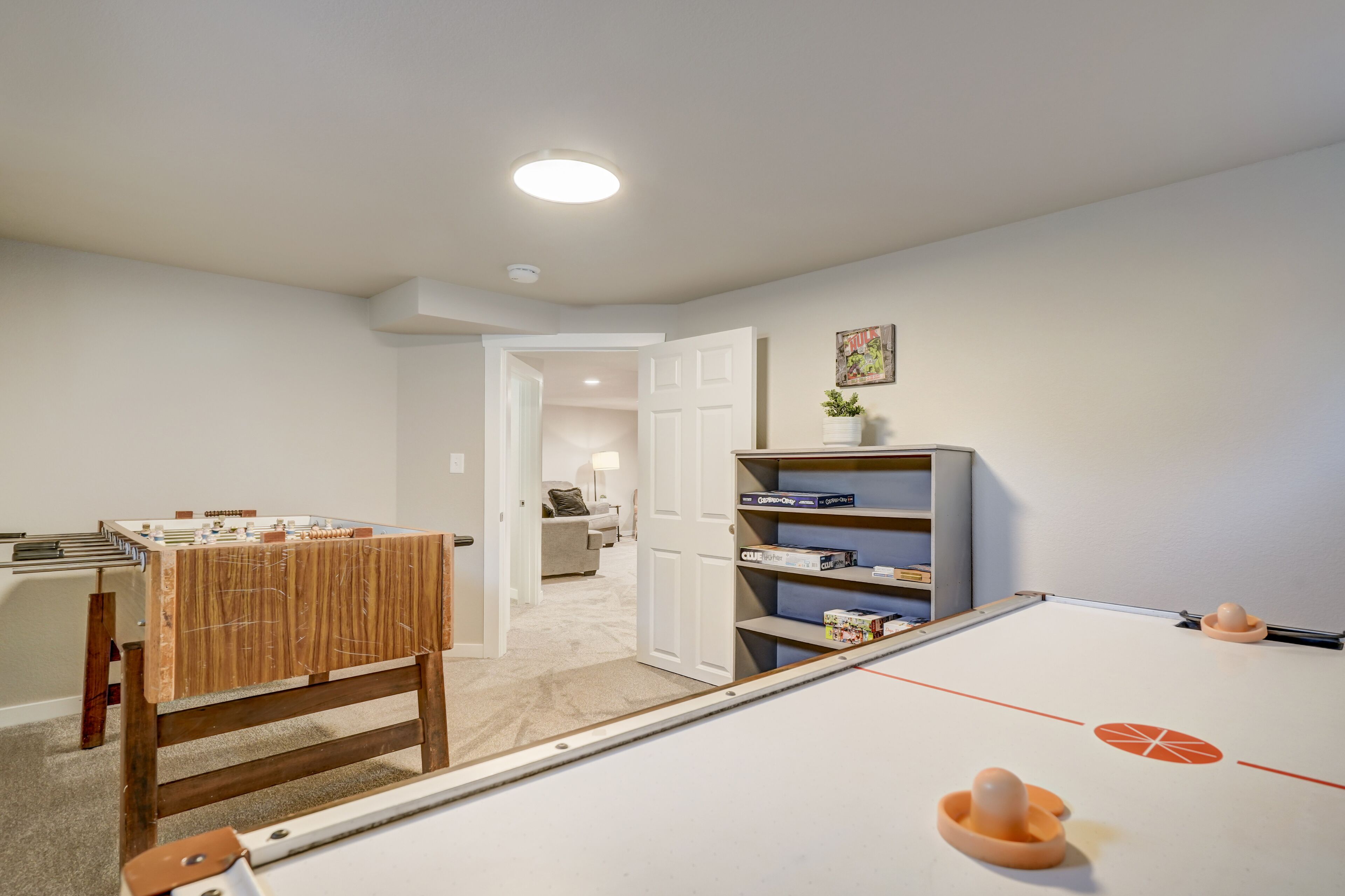 Une pièce avec une table de baby-foot, une bibliothèque et une porte donnant sur une autre pièce.
