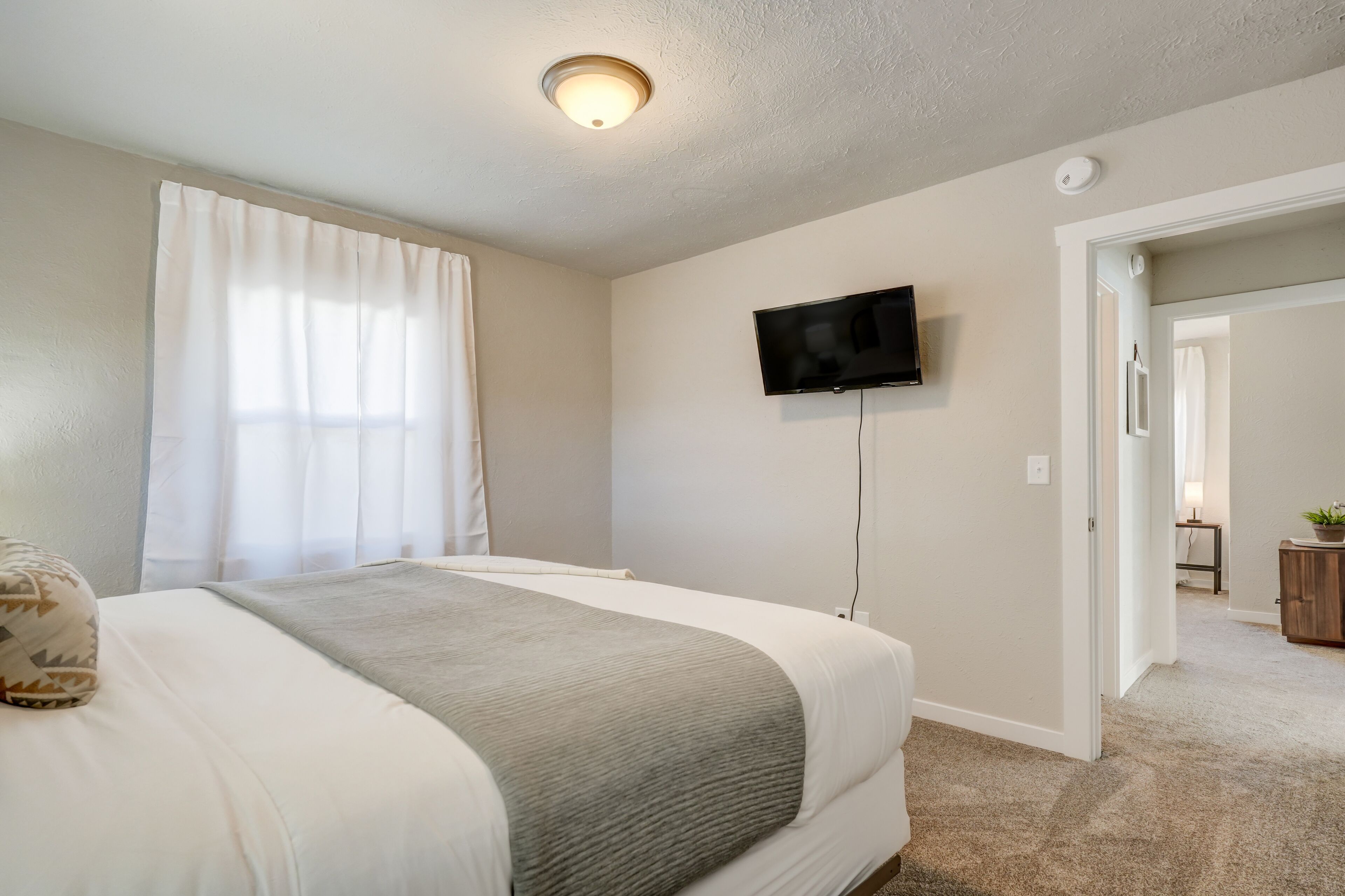 Une chambre à coucher avec un lit, un téléviseur fixé au mur et une porte donnant sur une autre pièce.
