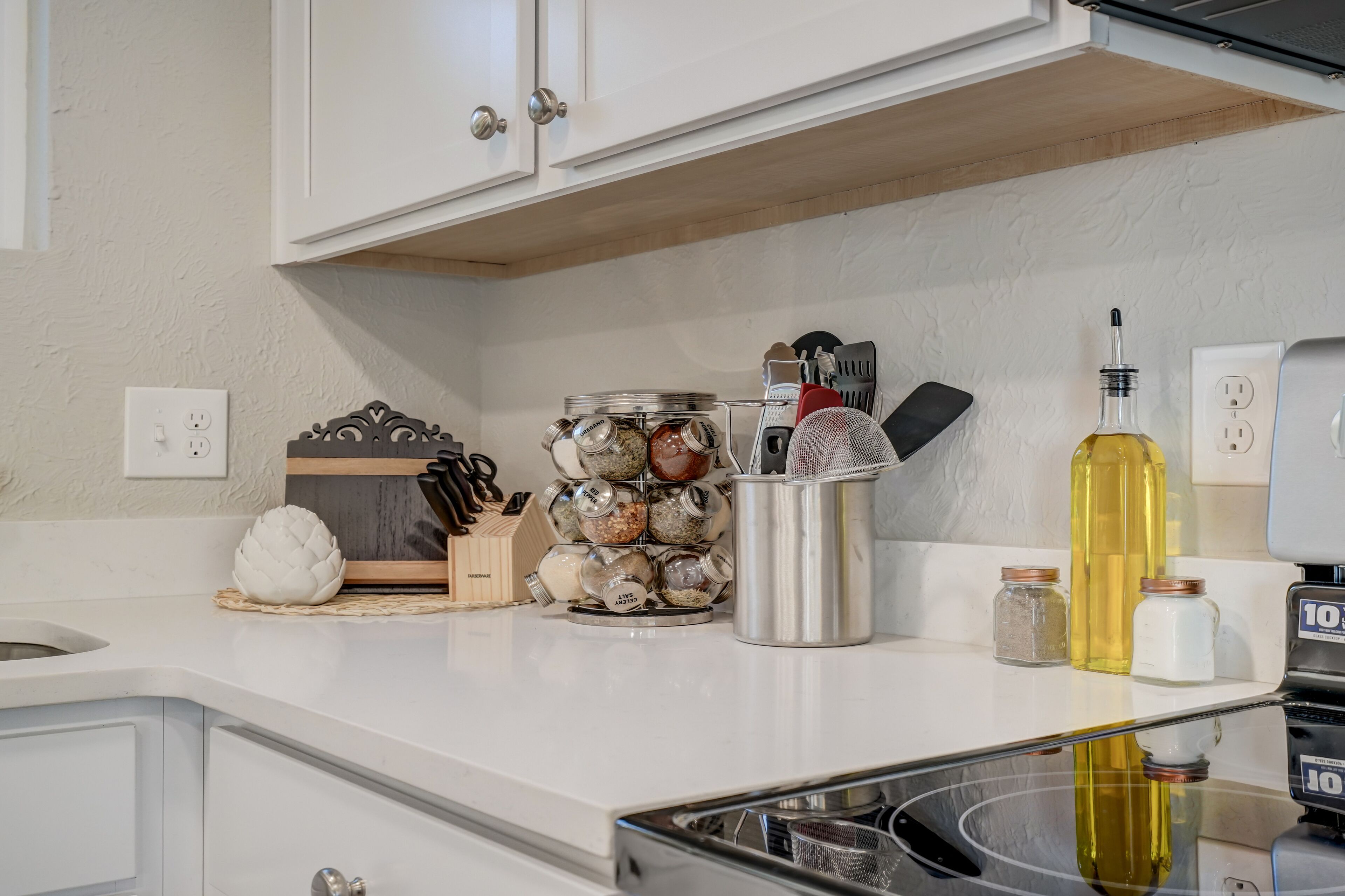 A kitchen with white cabinets, a countertop with jars of spices, a bottle of oil, and a meat grinder.