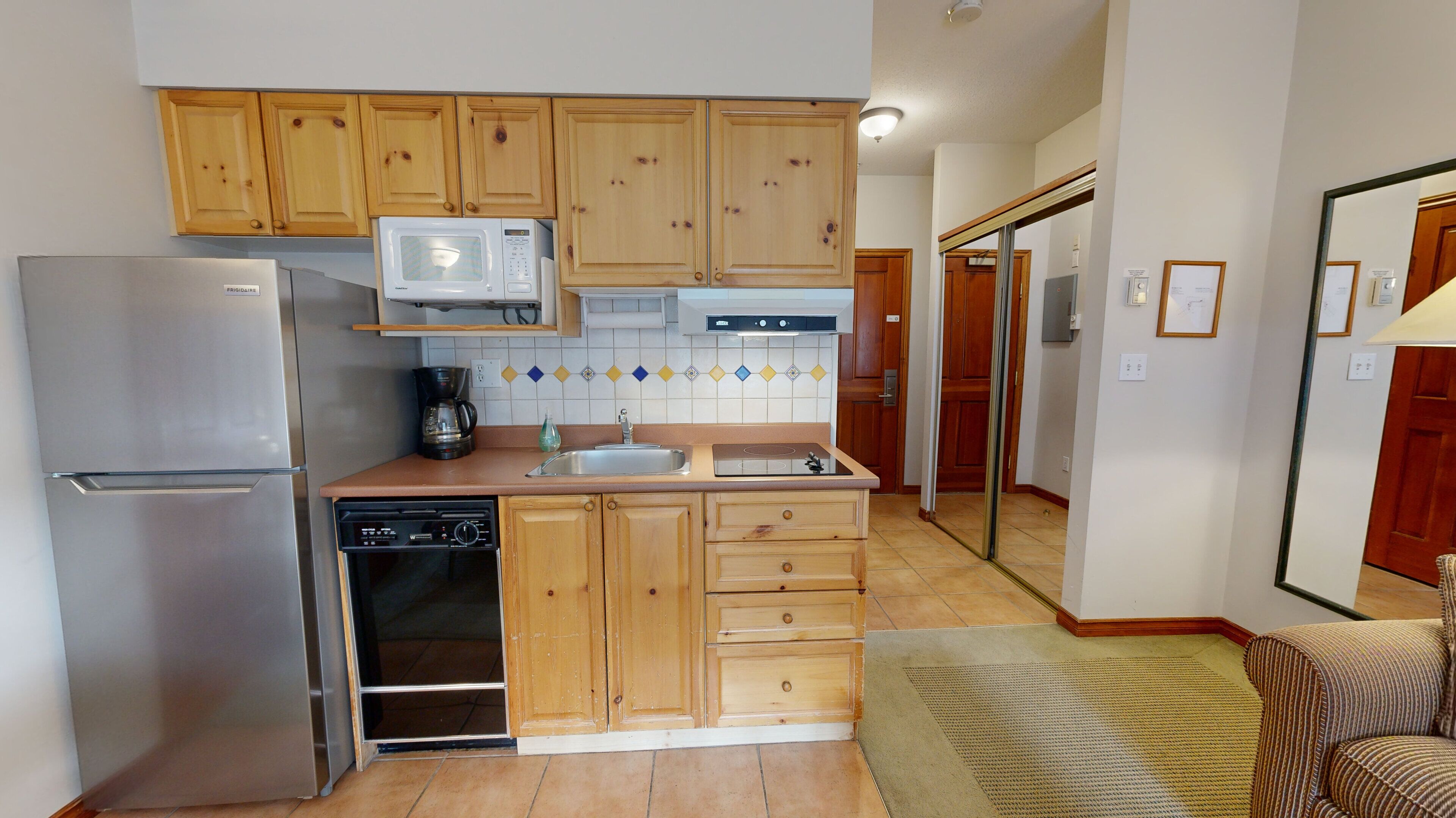 A compact kitchen with wooden cabinets, a stainless steel refrigerator, a microwave, a coffee maker, and a dishwasher.
