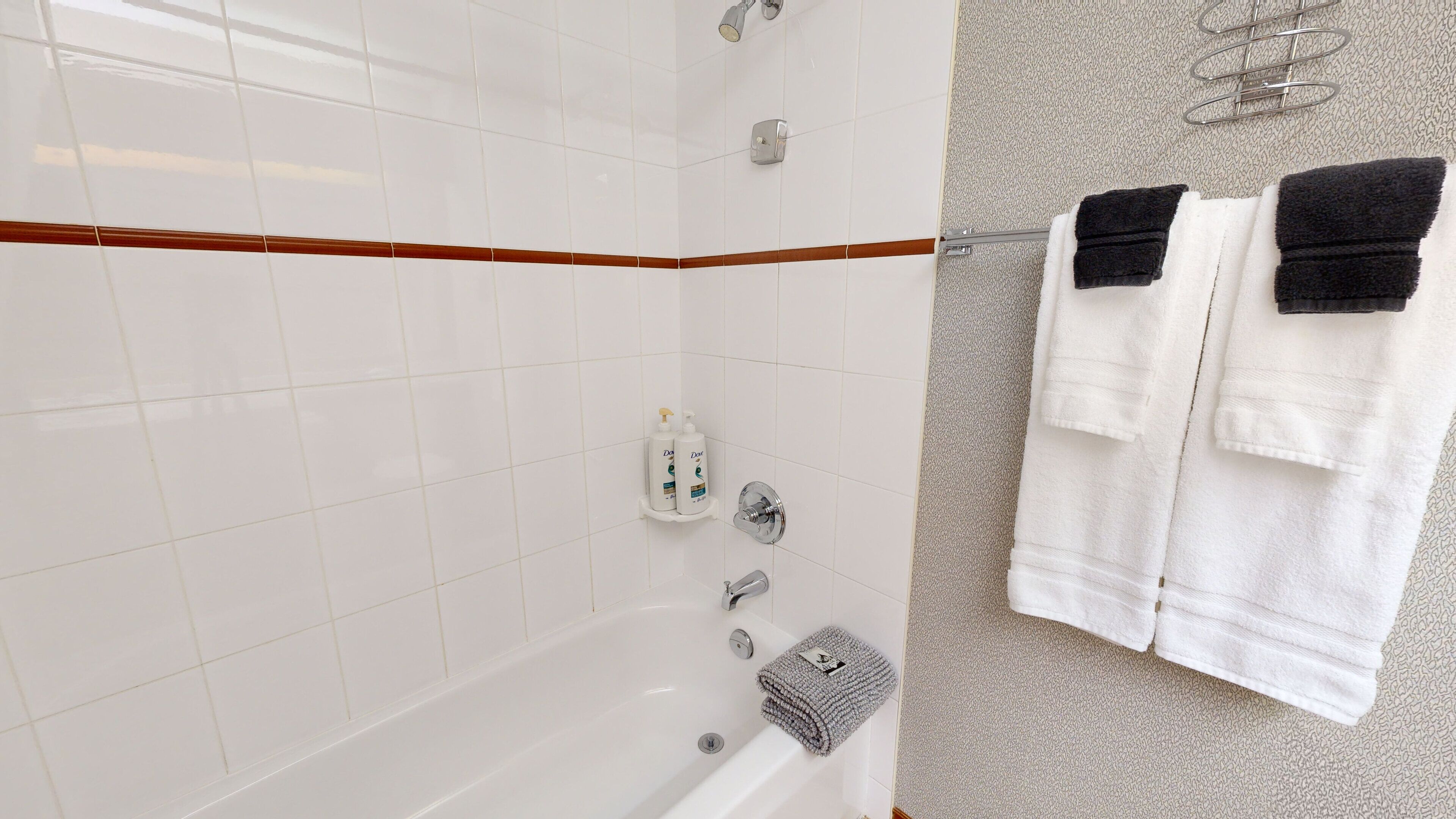 Ein Badezimmer mit weißen Fliesen, einer Badewanne, einer Dusche und einem Handtuchhalter mit Handtüchern.