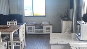 Une cuisine moderne avec des meubles blancs, une table à manger en bois et un coin salon comprenant un canapé et des fauteuils.