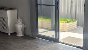 Un intérieur moderne avec une porte-fenêtre coulissante donnant sur un espace extérieur, un téléviseur à écran plat fixé au mur et un vase décoratif blanc.
