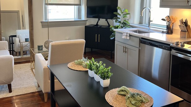 A modern kitchen with a dining area, featuring a large window, stainless steel appliances, and a flat-screen TV. - Serene Urban Oasis (Louisville)