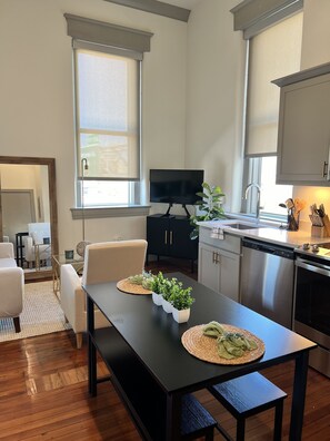 A modern kitchen with a dining area, featuring a large window, stainless steel appliances, and a flat-screen TV. - Serene Urban Oasis (Louisville)