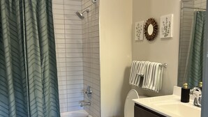 A bathroom with a bathtub, toilet, vanity, and a shower curtain. - Serene Urban Oasis (Louisville)