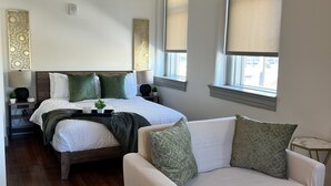 A modern bedroom with a large bed, a sofa, and a small table. - Serene Urban Oasis (Louisville)