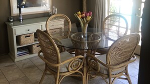 A dining area with a round glass table surrounded by wicker chairs, a ceiling fan, a potted plant, and a large mirror on the wall. - In the Heart of Palm Desert! (Palm Desert)