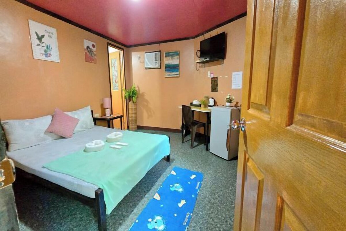 A bedroom with a bed, desk, and a television on the wall.