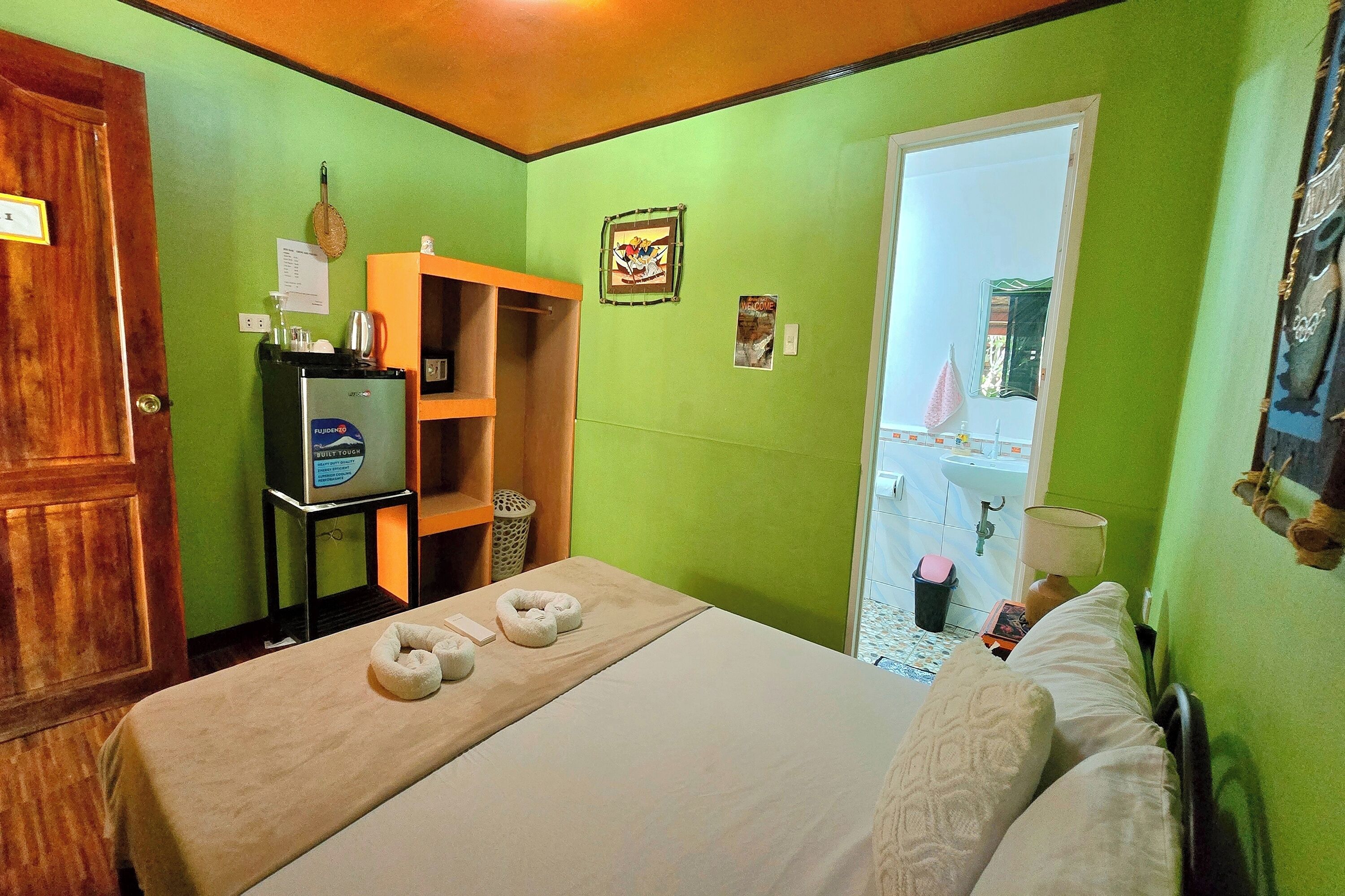 Quarto de hotel com uma cama, televisão sobre um suporte, porta de madeira e parede verde.