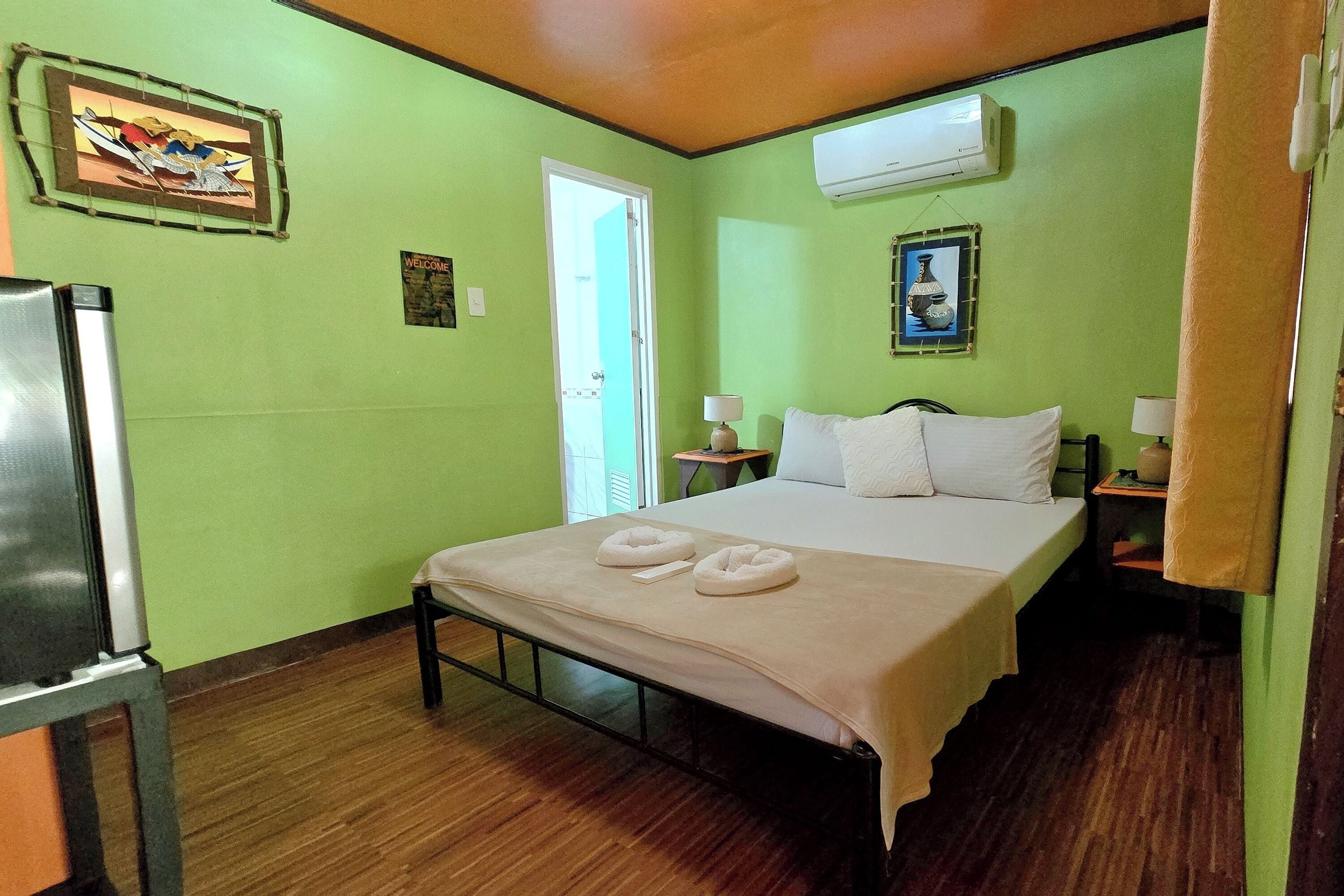 A room with a bed, a nightstand, a lamp, and a refrigerator.