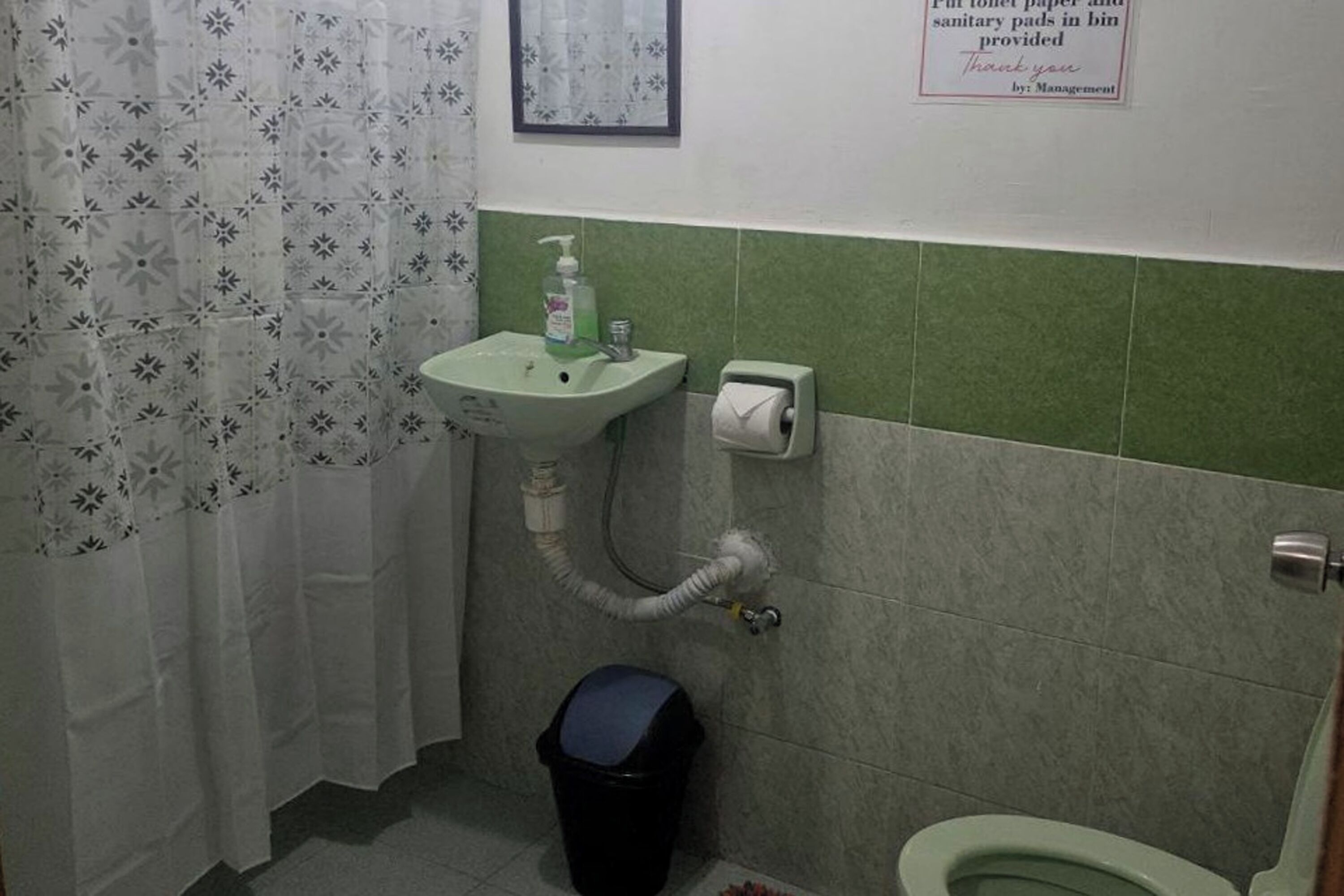 Ein Badezimmer mit Waschbecken, Toilette und Mülleimer. Ein Schild weist darauf hin, dass Toilettenpapier und Damenbinden im Mülleimer bereitstehen.
