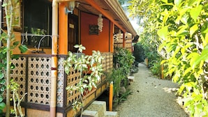 Uma casa de madeira tradicional com varanda coberta, cerca de bambu e caminho de cascalho.