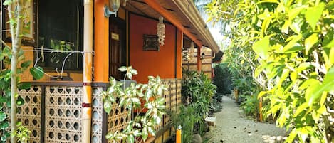 A traditional wooden house with a covered porch, a bamboo fence, and a gravel path.