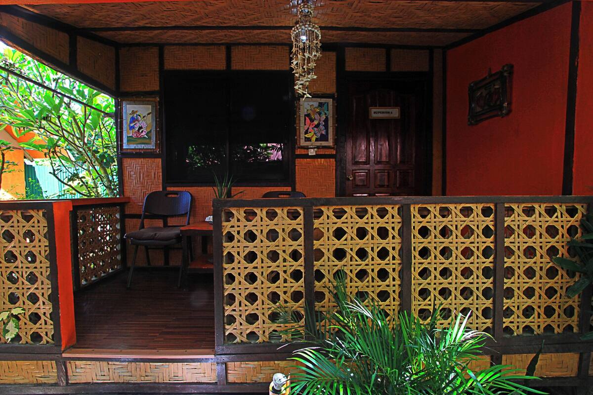 A room with a wooden ceiling, a wooden bench, a chair, and a potted plant.