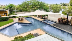 A swimming pool with a sunshade, surrounded by greenery and a small seating area. - City Stadium 2 (Townsville)