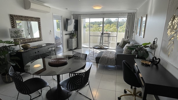 A modern living room with a dining area, a sofa, and a balcony with a view. - City Stadium 2 (Townsville)