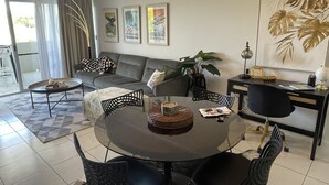 A modern living room with a grey sofa, a round dining table, and a black office chair. There are framed pictures on the wall, a potted plant, and a globe on the desk. - City Stadium 2 (Townsville)