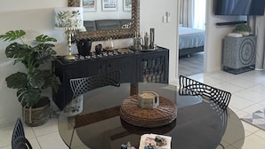 A modern living room with a round glass table, black chairs, a black sofa, a coffee table, a TV, and a large mirror on the wall. - City Stadium 2 (Townsville)