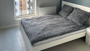 Ein Schlafzimmer mit Bett, Fenster, Heizkörper und einer Pendelleuchte.