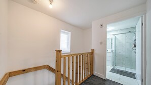 Un escalier avec des rampes en bois, un plancher recouvert de moquette et une porte de douche en verre donnant sur une salle de bain.
