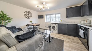 Un espace de vie compact comprenant un canapé, une table basse, un lave-linge, un téléviseur et un coin cuisine.