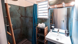Ein Badezimmer mit Dusche, Waschbecken, Spiegel und einem Fenster mit Jalousien.