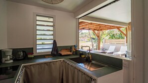 Eine Küche mit Spüle, einem Fenster mit Jalousien und Blick auf einen Außenbereich mit Sitzgelegenheiten.