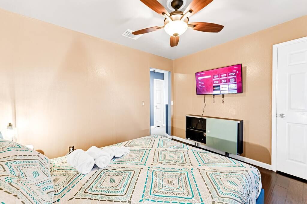 Ein Schlafzimmer mit einem Bett, einem Deckenventilator, einem an der Wand montierten Fernseher und einer Tür.