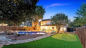 A backyard with a swimming pool, a putting green, and a wooden fence. - 5 BR w/pool, minutes to Six flags, AT&T stadium (Grand Prairie)