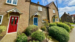 A row of brick houses with distinct red and blue doors, surrounded by well-maintained hedges and a clear sky.