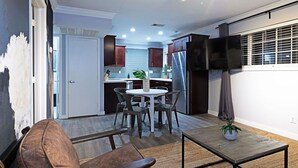 Une cuisine moderne avec des meubles de couleur sombre en bois, un réfrigérateur en acier inoxydable et un four encastré. On y trouve un coin repas avec une table ronde et des chaises, ainsi qu'une petite plante en pot posée sur une table en bois.
