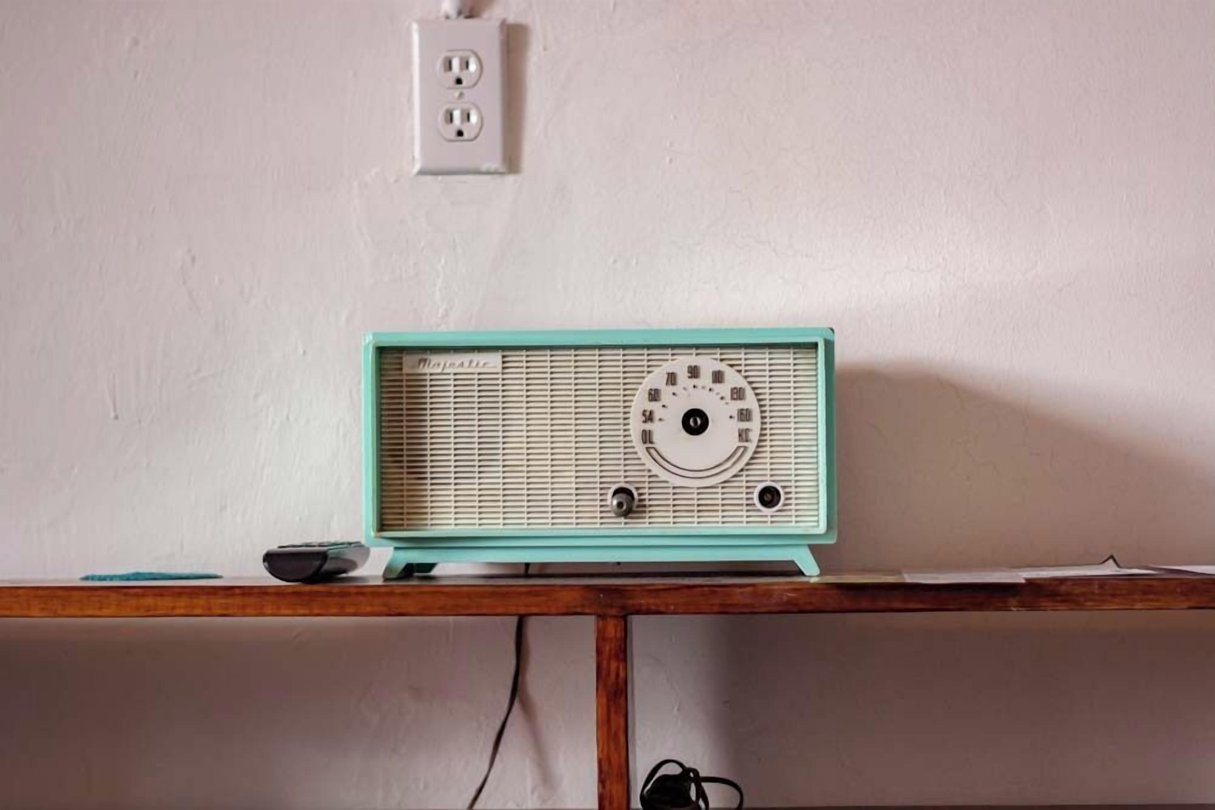 Sinivihreä radio puupöydällä valkoista seinää vasten.