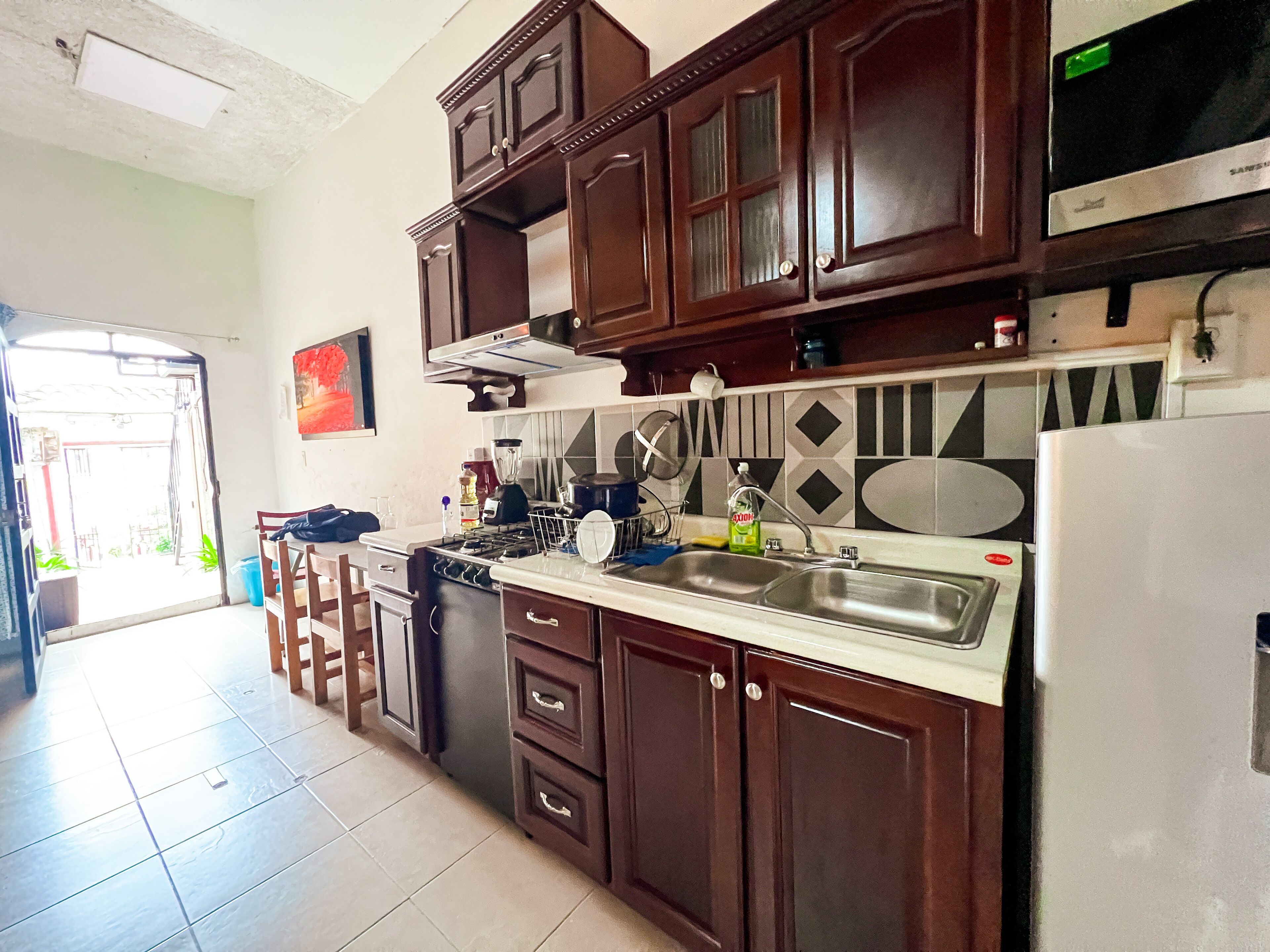 A kitchen with dark wooden cabinets, a stainless steel sink, and a refrigerator.