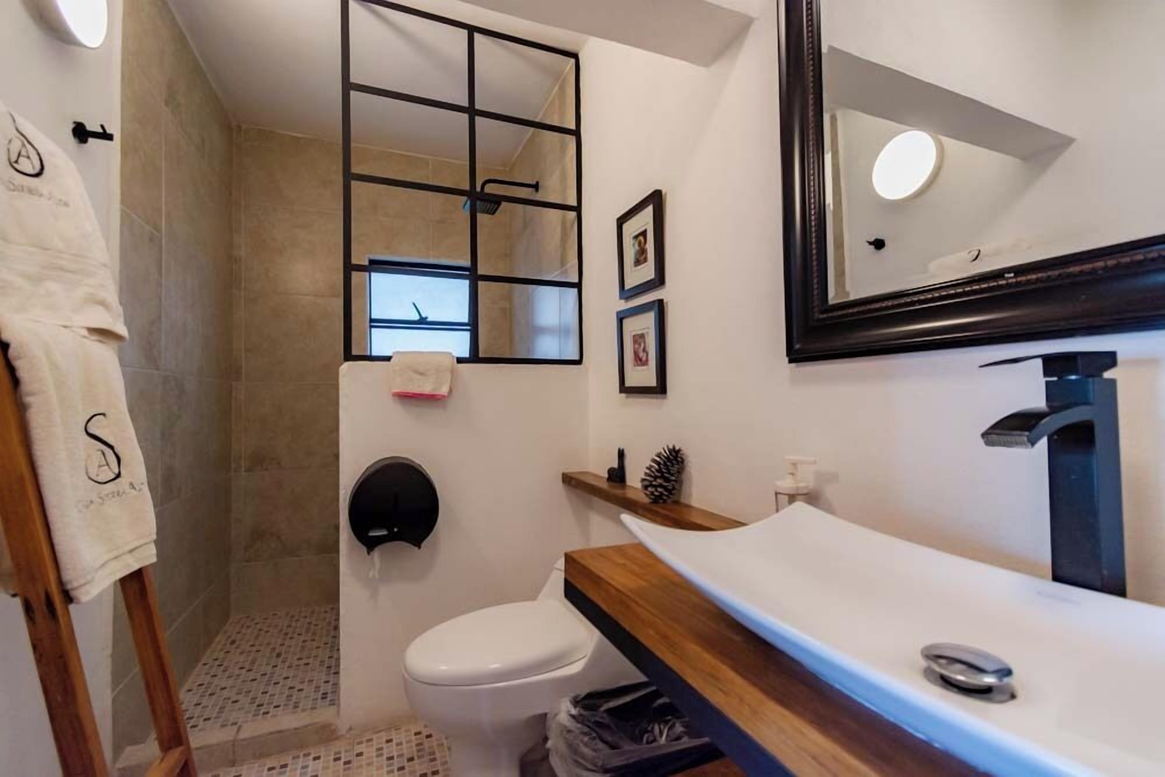 A bathroom with a shower, toilet, and sink. There is a towel rack, a mirror, and a shelf with toiletries.