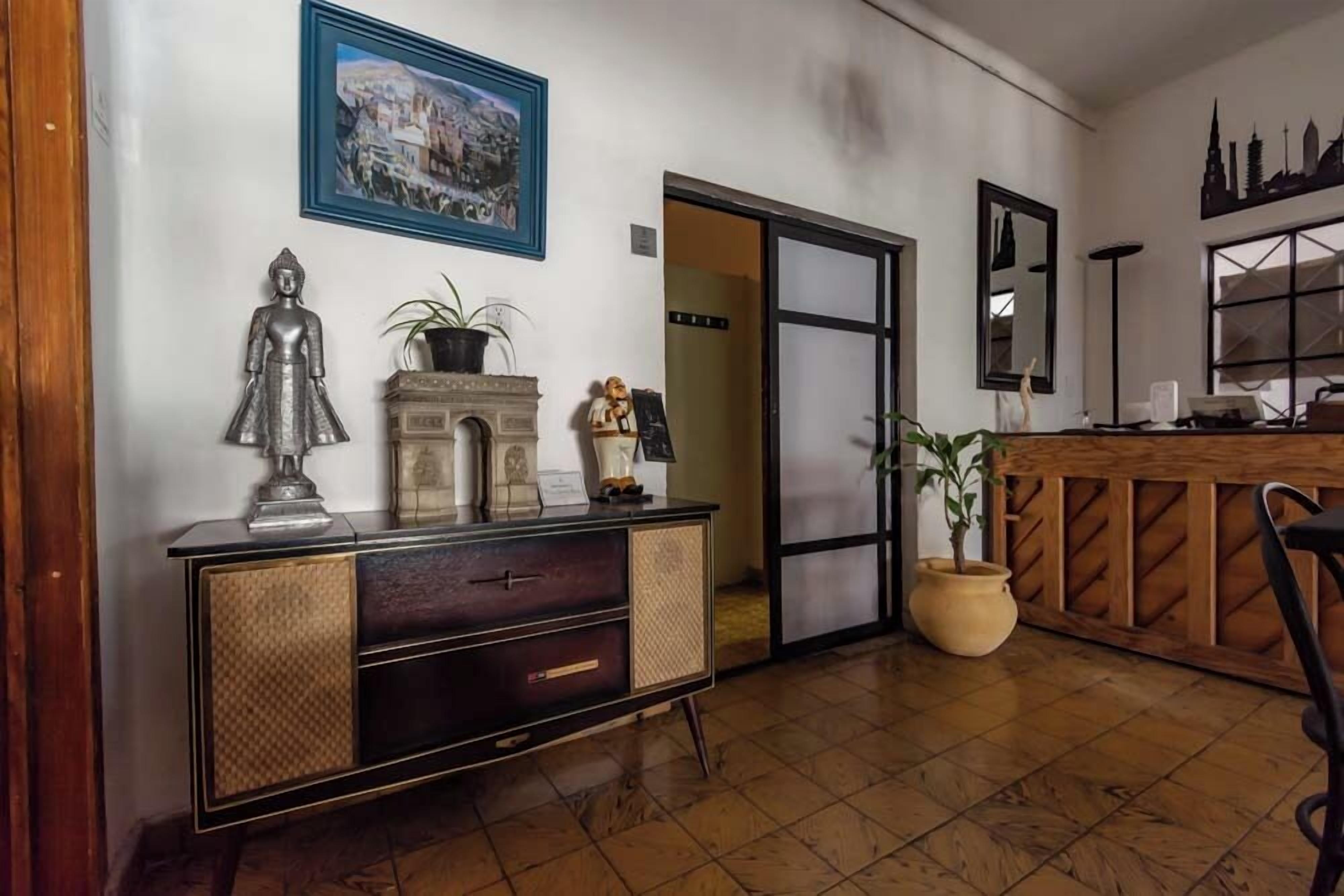 A room with a wooden floor, a dark wooden cabinet with drawers, a large potted plant, and a framed picture on the wall.